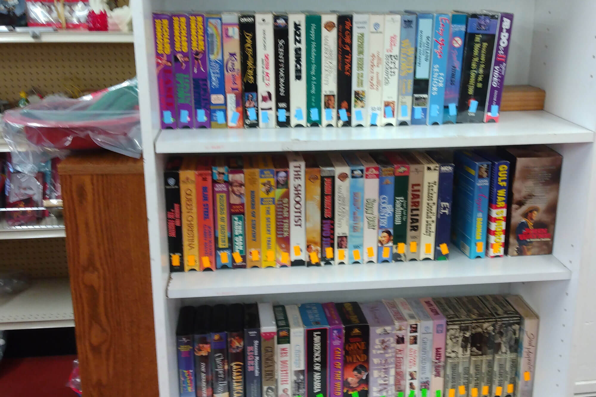 Image of VHS tapes on three shelves in a book case at a thrift store